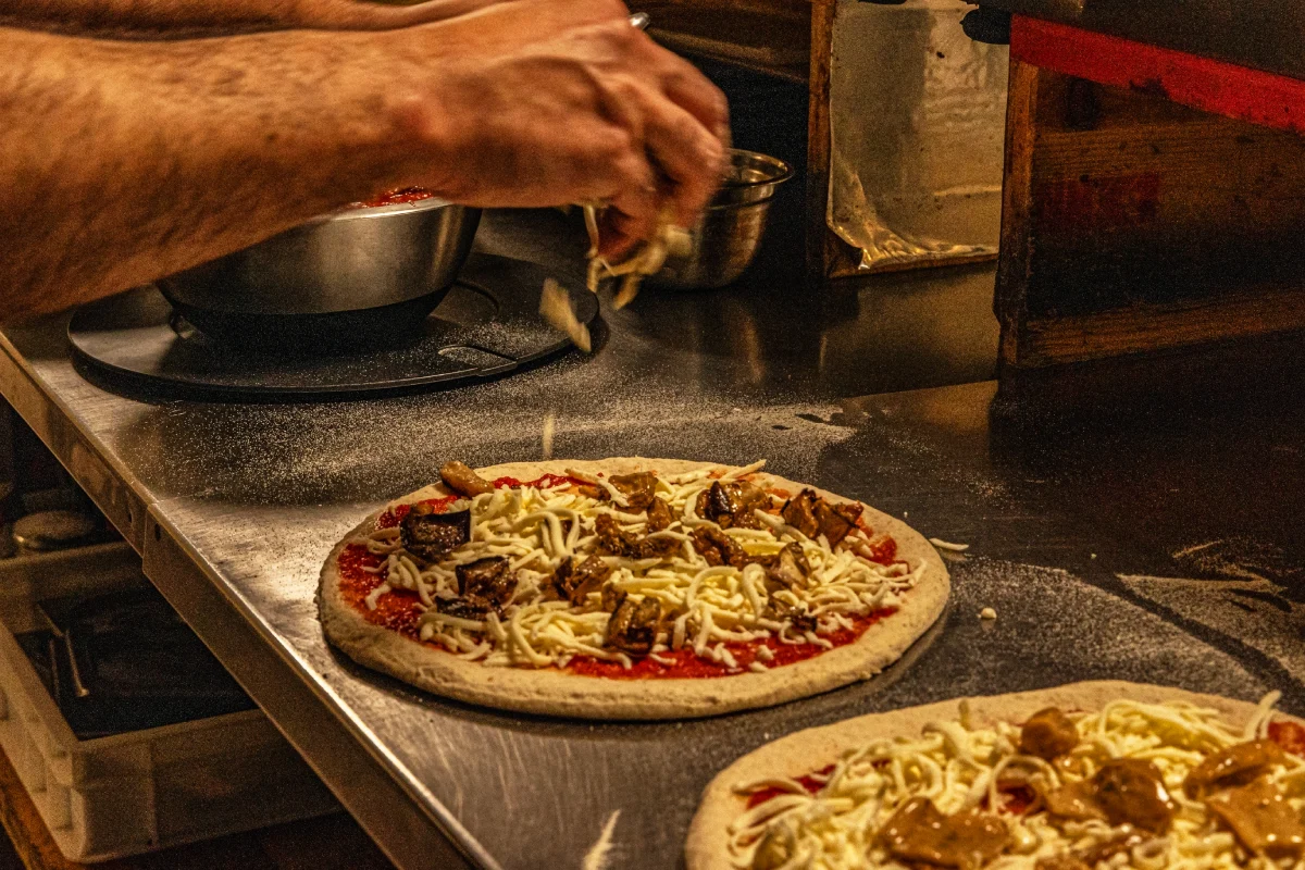 Chef del ristorante pizzeria Magie a Castelvetrano mentre condisce una pizza gourmet con ingredienti di qualità | Magie ristorante pizzeria a Castelvetrano